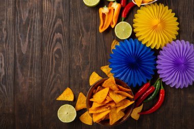 Cinco de Mayo (5 Mayıs) kutlama konsepti. Geleneksel Meksika cipsleriyle Meksika arka plan şenliği, kırmızı biber, koyu ahşap arka planda yeşil limon. Üst görünüm, alanı kopyala.