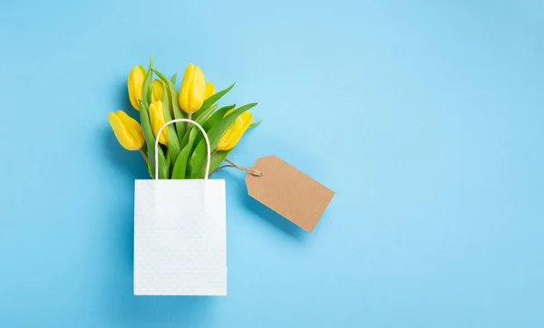 母の日 国際女性の日 バレンタインデーグリーティングカードの背景 青いテーブルの上の願いのための休日の春の黄色のチューリップの花花束とタグ トップビューのコピースペース — ストック写真