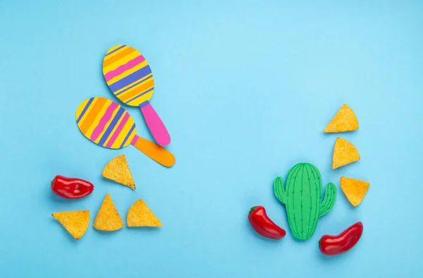 Mexican background fiesta with Traditional Mexican nachos chips, red chilli pepper, cactus and maracas on blue background. Cinco de Mayo (Fifth of May) celebration concept. Top view, copy space.