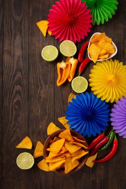 Cinco de Mayo (5 Mayıs) kutlama konsepti. Geleneksel Meksika cipsleriyle Meksika arka plan şenliği, kırmızı biber, koyu ahşap arka planda yeşil limon. Üst görünüm, alanı kopyala.