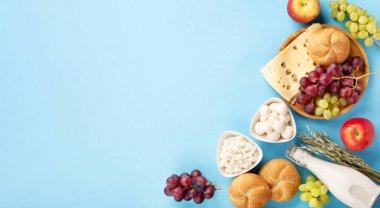 Mutlu Shavuot bayram kartları, Yahudi dini bayramı konsepti. Süt ürünleri, meyveler, peynir, ekmek, mavi arka planda süt şişesi. Düz konum, üst görünüm, kopyalama alanı.