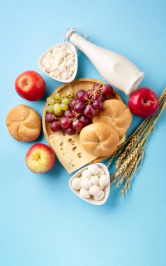Mutlu Shavuot bayram kartları, Yahudi dini bayramı konsepti. Süt ürünleri, meyveler, peynir, ekmek, mavi arka planda süt şişesi. Düz konum, üst görünüm, kopyalama alanı.