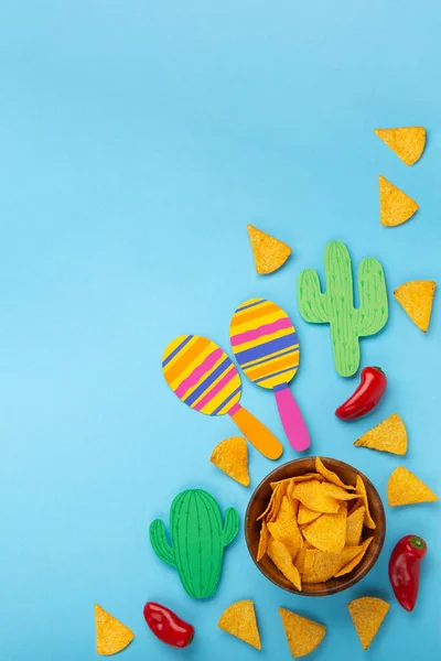Mexican background fiesta with Traditional Mexican nachos chips, red chilli pepper, cactus and maracas on blue background. Cinco de Mayo (Fifth of May) celebration concept. Top view, copy space.
