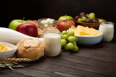 Mutlu Shavuot şenlik kartları. Yahudi dini bayramı konsepti. Süt ürünleri, meyveler, peynir, ekmek, süt şişesi, süzme peynir, koyu ahşap arka planda buğday. Üst görünüm, alanı kopyala.