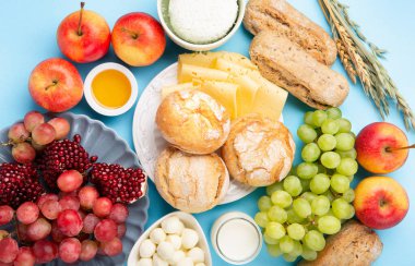 Mutlu Shavuot şenlik kartları. Yahudi dini bayramı konsepti. Süt ürünleri, üzüm, peynir, ekmek, süt, süzme peynir, buğday, mavi arka planda bal. Üst görünüm.