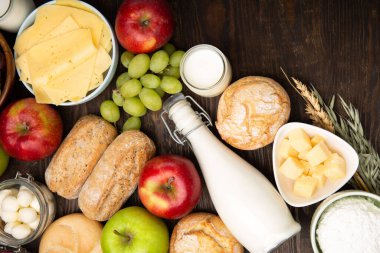 Mutlu Shavuot şenlik kartları. Yahudi dini bayramı konsepti. Süt ürünleri, meyveler, peynir, ekmek, süt şişesi, süzme peynir, koyu ahşap arka planda buğday. Üst görünüm, alanı kopyala.