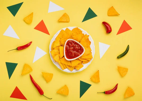 stock image Mexican fiesta background with Traditional Mexican nachos chips, chilli peppers and tomato salsa sauce on yellow background. Cinco de Mayo (Fifth of May) celebration concept. Top view, copy space.