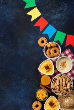 Junina Yaz Festivali Karnavalı konsepti. Brezilya hasır şapkası, Mısır keki, yer fıstığı ve ahşap mavi arka planda renkli bayraklar, üst manzara. Tebrik Kartı, Davetiye veya Tatil Posteri Tasarımı