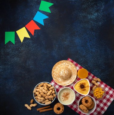 Junina Yaz Festivali Karnavalı konsepti. Brezilya hasır şapkası, Mısır keki, yer fıstığı ve ahşap mavi arka planda renkli bayraklar, üst manzara. Tebrik Kartı, Davetiye veya Tatil Posteri Tasarımı