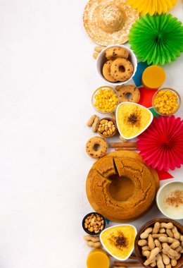 Junina Yaz Festivali Karnavalı konsepti. Brezilya hasır şapkası, Mısır keki, fıstık ve beyaz ahşap arka planda renkli bayraklar, üst manzara. Tebrik Kartı, Davetiye veya Tatil Posteri Tasarımı