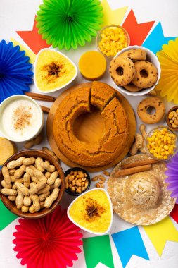 Junina Yaz Festivali Karnavalı konsepti. Brezilya hasır şapkası, Mısır keki, fıstık ve beyaz ahşap arka planda renkli bayraklar, üst manzara. Tebrik Kartı, Davetiye veya Tatil Posteri Tasarımı