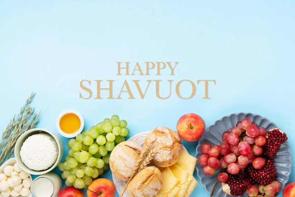 Stock image Happy Shavuot festive card. Jewish religious holiday concept. Dairy products, grapes, cheese, bread, milk, cottage cheese, wheat, honey on blue background. Top view, copy space.