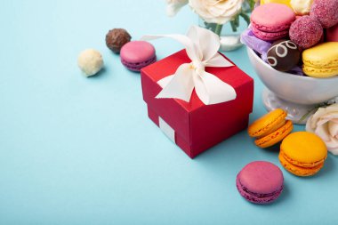 Tatlı kurabiyeler, kırmızı hediye kutusu, gül çiçekleri ve mavi arka planda çikolatalı şekerler. Bahar Anneler Günü için hediye konsepti, kadınlar günü, doğum günü. Düz konum, mesaj veya metin için boş boşluk