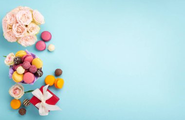 Tatlı kurabiyeler, kırmızı hediye kutusu, gül çiçekleri ve mavi arka planda çikolatalı şekerler. Bahar Anneler Günü için hediye konsepti, kadınlar günü, doğum günü. Düz konum, mesaj veya metin için boş boşluk