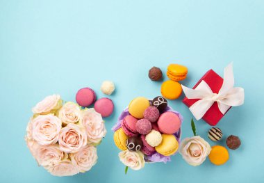 Tatlı kurabiyeler, kırmızı hediye kutusu, gül çiçekleri ve mavi arka planda çikolatalı şekerler. Bahar Anneler Günü için hediye konsepti, kadınlar günü, doğum günü. Düz konum, mesaj veya metin için boş boşluk