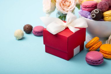 Tatlı kurabiyeler, kırmızı hediye kutusu, gül çiçekleri ve mavi arka planda çikolatalı şekerler. Bahar anneler günü, kadınlar günü, doğum günü, mesaj veya mesaj için boş alan sunar