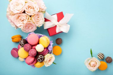 Tatlı kurabiyeler, kırmızı hediye kutusu, gül çiçekleri ve mavi arka planda çikolatalı şekerler. Bahar Anneler Günü için hediye konsepti, kadınlar günü, doğum günü. Düz konum, mesaj veya metin için boş boşluk