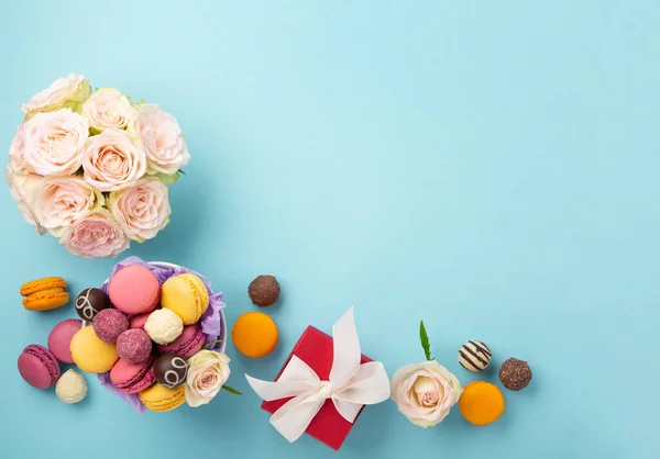 甘いクッキーマカロン 赤いギフトボックス 青の背景にバラの花とチョコレートキャンディー 春は母の日 女性の日 誕生日のための概念を提示します フラットレイアウト テキストやメッセージのための空のスペース — ストック写真