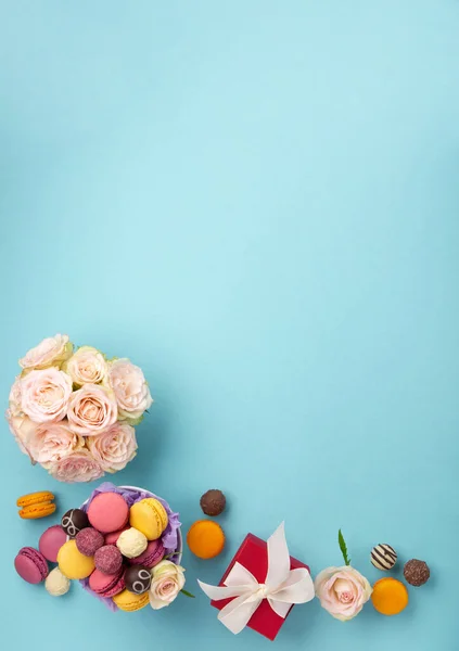 甘いクッキーマカロン 赤いギフトボックス 青の背景にバラの花とチョコレートキャンディー 春は母の日 女性の日 誕生日のための概念を提示します フラットレイアウト テキストやメッセージのための空のスペース — ストック写真