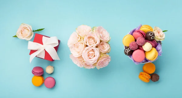 甘いクッキーマカロン 赤いギフトボックス 青の背景にバラの花とチョコレートキャンディー 春は母の日 女性の日 誕生日のための概念を提示します トップビュー コピースペース — ストック写真