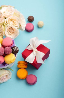 Tatlı kurabiyeler, kırmızı hediye kutusu, gül çiçekleri ve mavi arka planda çikolatalı şekerler. Bahar Anneler Günü için hediye konsepti, kadınlar günü, doğum günü. Düz konum, mesaj veya metin için boş boşluk
