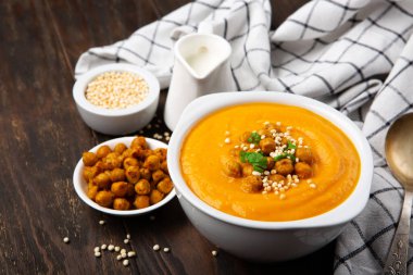 Sonbahar vejetaryen balkabağı ve havuç kremalı çorba, nohut ve siyah ahşap arka planda otlar. Rahatlatıcı yiyecekler, sonbahar ve kış sağlıklı yavaş yemek konsepti.