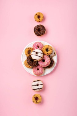 Pembe arka planda çikolata ve şeker serpiştirilmiş renkli çörekler, üst manzara. Karnaval ya da doğum günü partisi kartı. Ulusal Çörek Gününüz kutlu olsun.. 