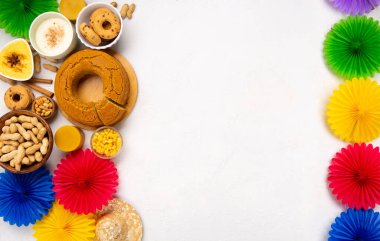 Junina Yaz Festivali Karnavalı konsepti. Brezilya hasır şapkası, Mısır keki, fıstık ve beyaz ahşap arka planda renkli bayraklar, üst manzara. Tebrik Kartı, Davetiye veya Tatil Posteri Tasarımı