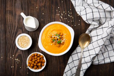 Sonbahar vejetaryen balkabağı ve havuç kremalı çorba, nohut ve siyah ahşap arka planda otlar. Rahatlatıcı yiyecekler, sonbahar ve kış sağlıklı yavaş yemek konsepti.