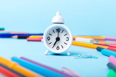 Okula, sınava, mavi arka planda eğitim konseptine. Okul dağınık kırtasiye malzemeleri, not defterleri, kalemler, ataçlar ve mavi masada beyaz alarm saati, kopyalama alanı. 