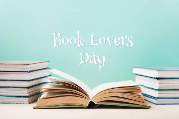 Book Lovers Day, Education concept. Open Book on wooden table and Stack of books on blue mint background. Festive card for books holiday, copy space.