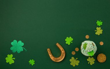 St. Patrick Günü vanilyalı ve yeşil kaplamalı çikolatalı kekler ve yeşil kağıt arka planda parlak yonca süslemeleri. İrlanda bayramı tatlı konsepti. Üst görünüm, alanı kopyala. 