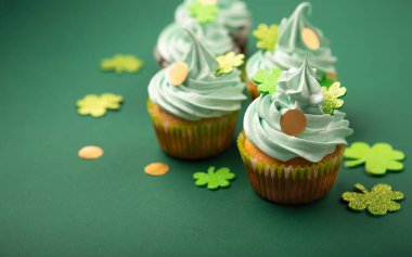 St. Patrick Günü vanilyalı ve yeşil kaplamalı çikolatalı kekler ve yeşil kağıt arka planda parlak yonca süslemeleri. İrlanda bayramı tatlı konsepti, kopyalama alanı. 