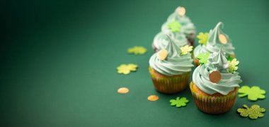 St. Patrick Günü vanilyalı ve yeşil kaplamalı çikolatalı kekler ve yeşil kağıt arka planda parlak yonca süslemeleri. İrlanda bayramı tatlı konsepti, kopyalama alanı. 