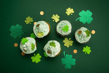 St. Patrick Günü vanilyalı ve yeşil kaplamalı çikolatalı kekler ve yeşil kağıt arka planda parlak yonca süslemeleri. İrlanda bayramı tatlı konsepti. Üst görünüm, alanı kopyala. 