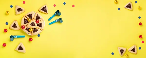 巧克力蘸着哈曼曲奇饼 狂欢节面具 吵闹者 甜糖果和黄色背景的节日派对装饰 俯瞰全景 纯正庆祝犹太人节日的概念 图库图片