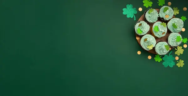 圣帕特里克节 Patrick Day 节日香草巧克力杯蛋糕 绿色糖霜 绿纸背景上有闪亮的三叶草装饰 爱尔兰假日甜点的概念 顶部视图 复制空间 免版税图库照片