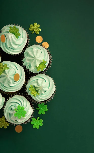セントパトリックの日のお祝いバニラチョコレートカップケーキ緑のフロスティングと光沢のあるクローバーの装飾グリーンペーパー背景 アイルランドの休日のデザートコンセプト トップビュー コピースペース ロイヤリティフリーのストック写真
