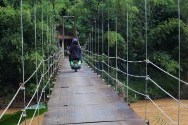Sukabumi, Batı Java, Endonezya 'da sabah üstü motosikletli köprüden geçen asma köprü. Geleneksel altyapı binaları.