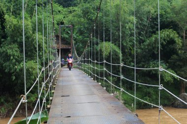 Sukabumi, Batı Java, Endonezya 'da sabah üstü motosikletli köprüden geçen asma köprü. Geleneksel altyapı binaları.
