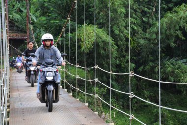 Sukabumi, Batı Java, Endonezya 'da sabah üstü motosikletli köprüden geçen asma köprü. Geleneksel altyapı binaları.