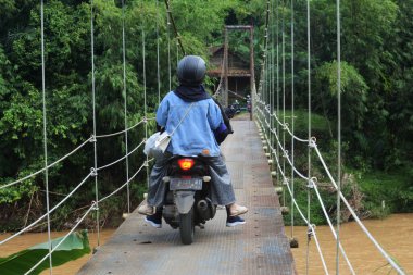Sukabumi, Batı Java, Endonezya 'da sabah üstü motosikletli köprüden geçen asma köprü. Geleneksel altyapı binaları.