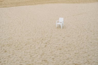Beach in winter deserted with an abandoned plastic white chair, rubbish in nature.