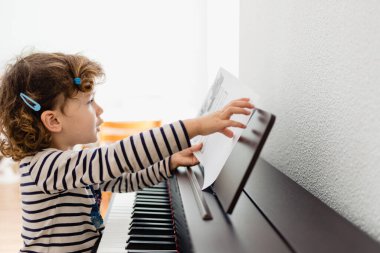 Kız piyano öğrencisi pratik yapmak için piyanosuna bir nota koyar.