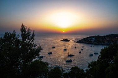 Güneşli sıcak bir gün batımı denizin yüzeyine yansıyor, körfezin yanında teknelerle..