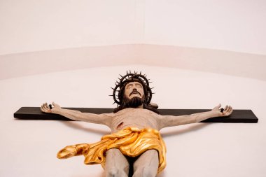 Çarmıha gerilmiş bir İsa heykeli, beyaz bir duvarda, aşağıdan görülüyor..