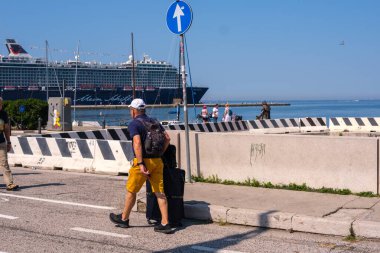 Trieste, İtalya 28-7-2024: Turistler güneşli bir günde İtalya 'nın Trieste kentinde demirlemiş bir yolcu gemisinin yanında yürüyorlar.