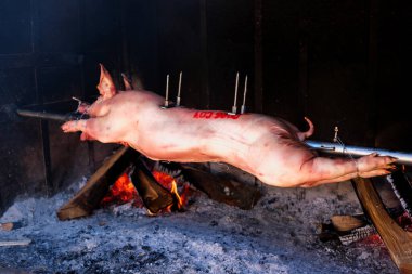 Yavru domuz, ızgaranın közlerinin üzerinde dönen bir çubuğa geçirilmiş.