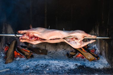 Yavru domuz, ızgaranın közlerinin üzerinde dönen bir çubuğa geçirilmiş.