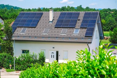 Güneşli bir günde yeşil bir çevrede güneş panelleri olan tek bir aile evi..